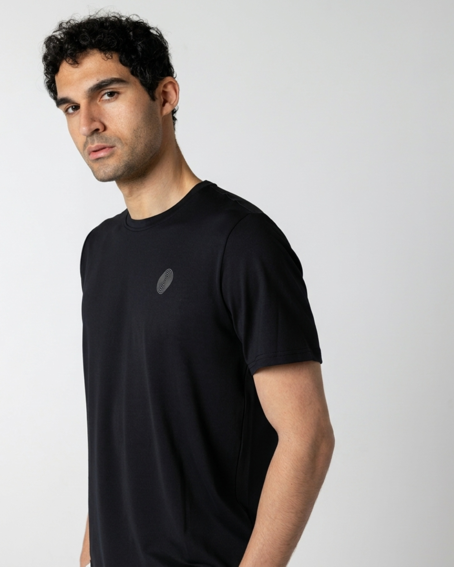 Man wearing a black t-shirt with a small logo on a light gray background