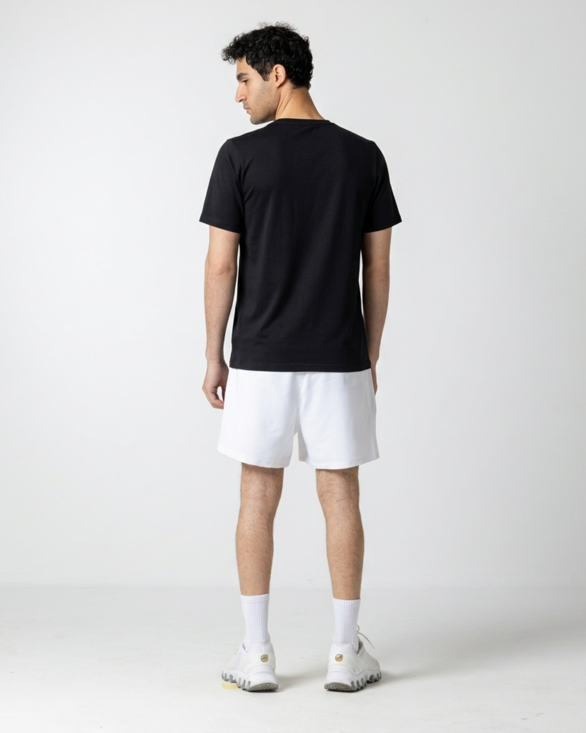 Person wearing a black t-shirt and white shorts on a plain background